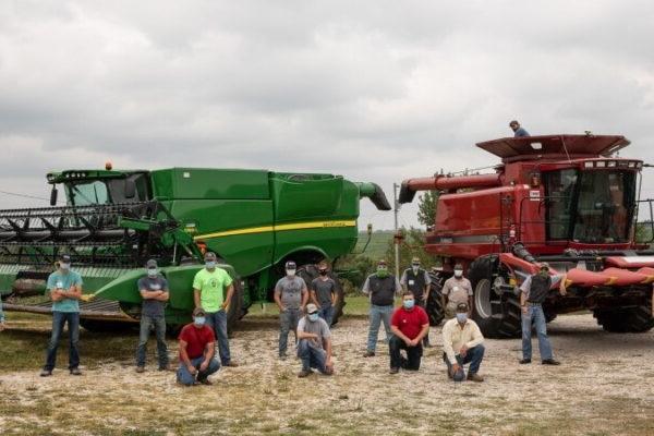 People in masks in front of farming equipment